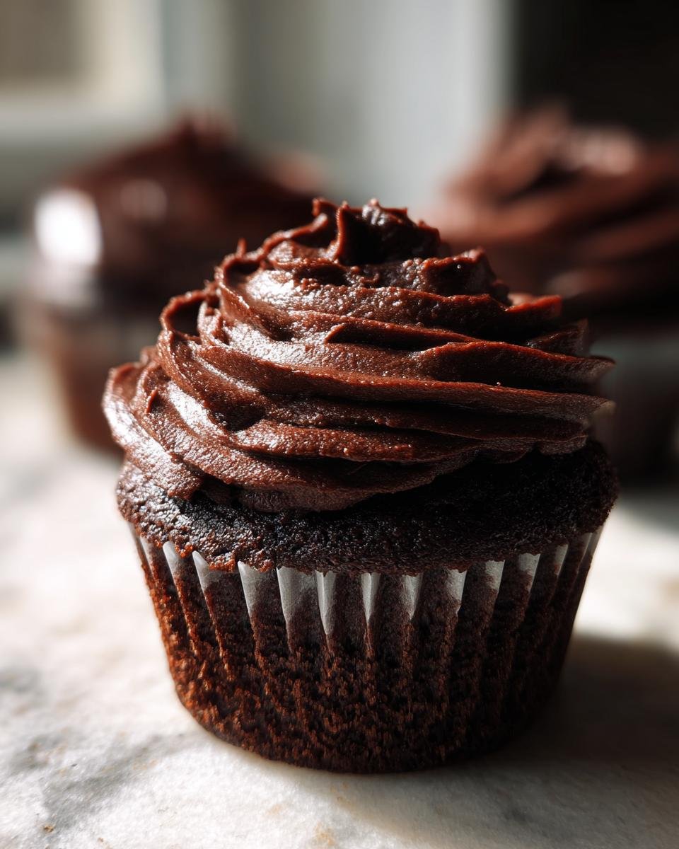 Nahaufnahme eines saftigen Spooky Double Chocolate Cupcakes mit dunkler Schokoladencreme.