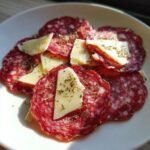 Nahaufnahme von Salami Scheiben mit K&auml;sest&uuml;cken und getrockneten Kr&auml;utern, ideal f&uuml;r Salami Rezepte.