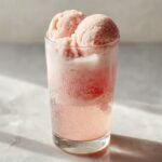 Zwei Kugeln rosafarbenes Sorbet schwimmen in einem sprudelnden Getr&auml;nk in einem hohen Glas &ndash; ein perfekter Sorbet Rose Floats.
