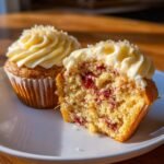 Nahaufnahme von Sparkling Cranberry White Chocolate Cupcakes, einer angeschnitten, um die saftige F&uuml;llung mit Cranberries zu zeigen.