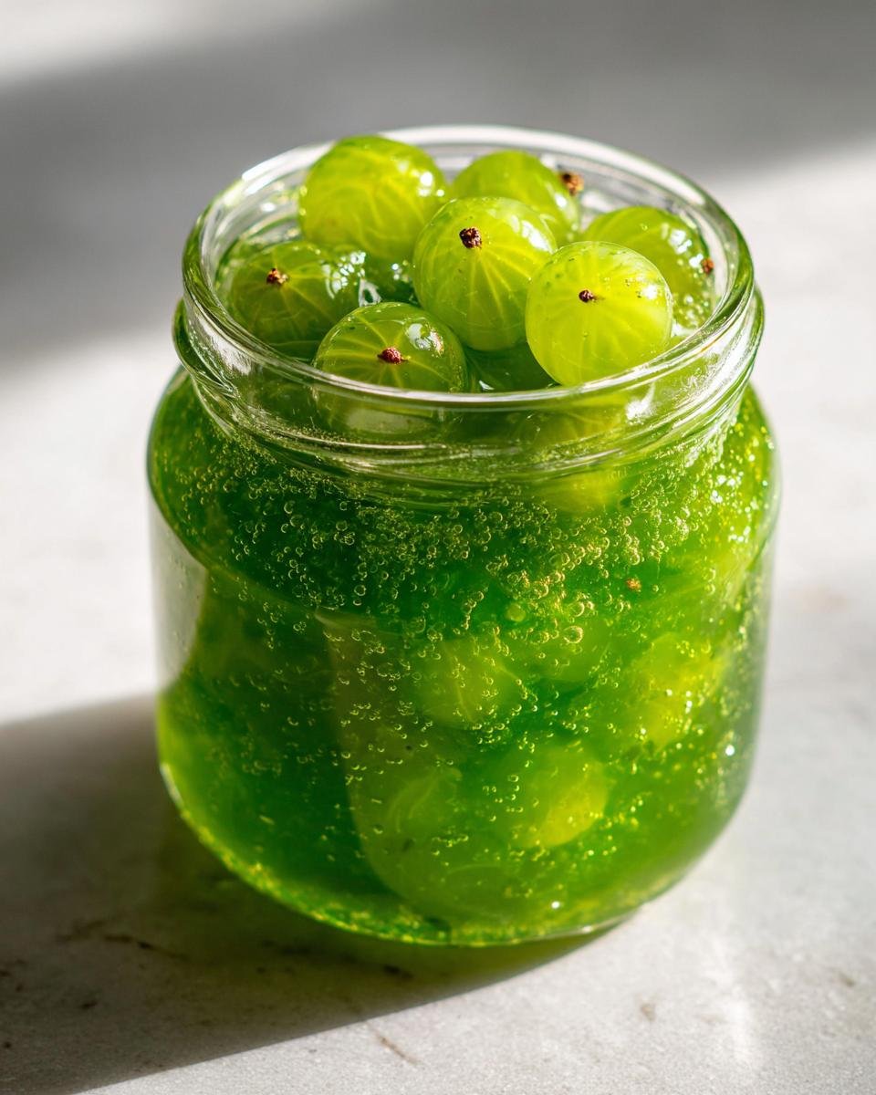 Nahaufnahme von frischen, gr&uuml;nen Stachelbeeren in einem Glas mit sprudelndem, leuchtend gr&uuml;nem Gelee.