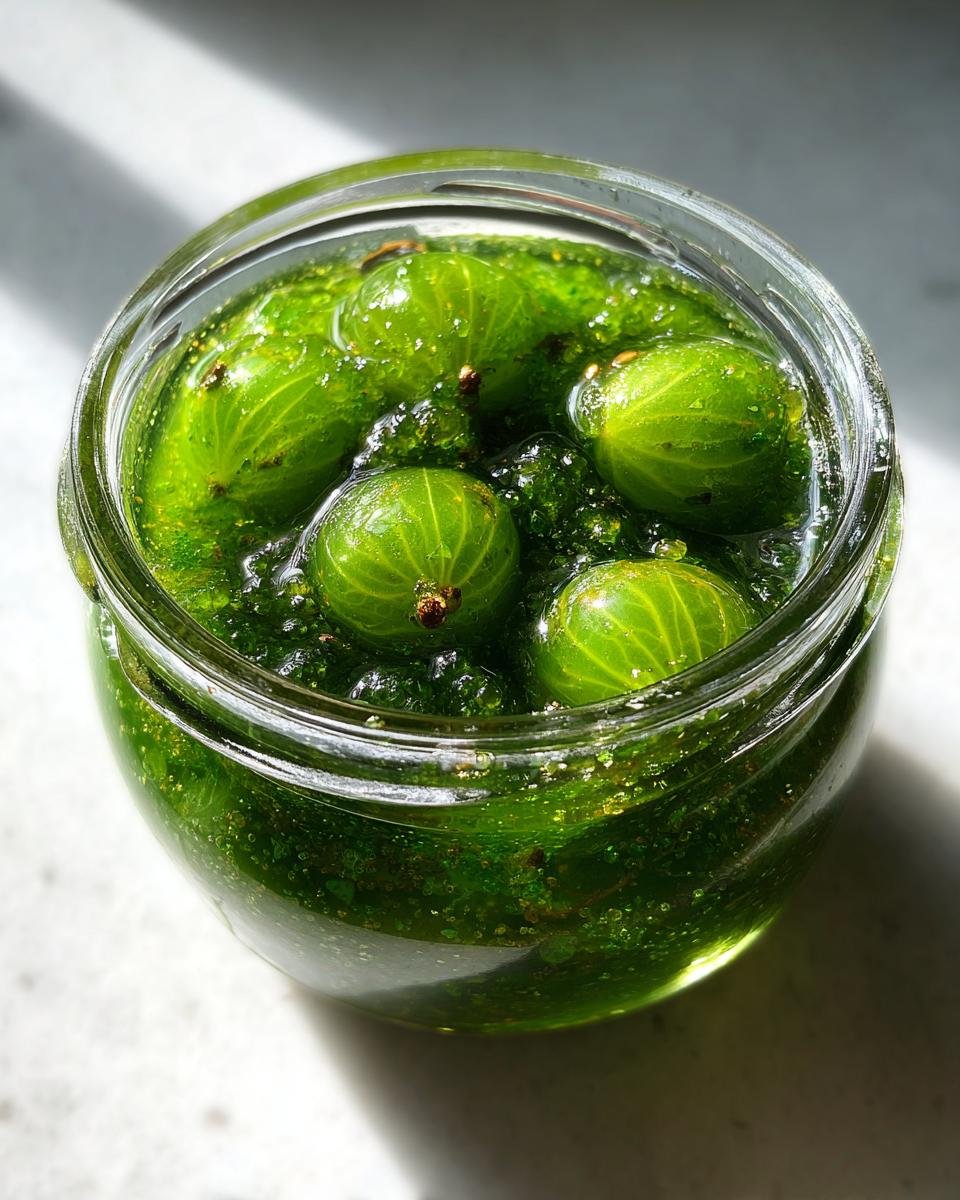 Nahaufnahme von ganzen, gr&uuml;nen Stachelbeeren in einer dickfl&uuml;ssigen, gr&uuml;nen Marmelade in einem Glas, typisch f&uuml;r Stachelbeeren Rezepte.