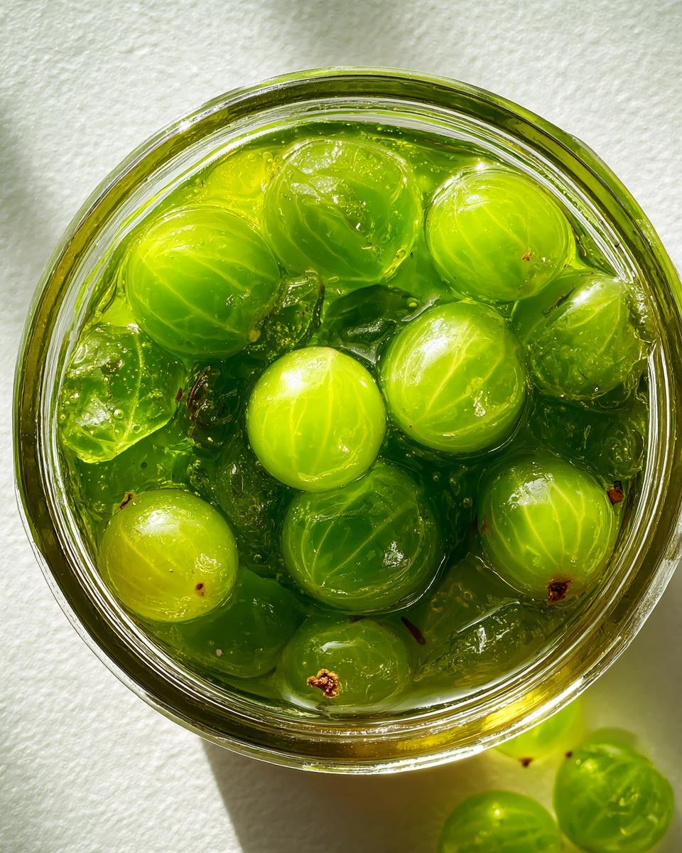 Nahaufnahme von gr&uuml;nen Stachelbeeren in einer hellgr&uuml;nen Marmelade in einem Glas, typisch f&uuml;r Stachelbeeren Rezepte.