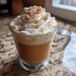 Nahaufnahme eines Starbucks Cinnamon Dolce Latte in einer Glastasse mit viel Schlagsahne und Zimt.