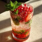 Nahaufnahme eines erfrischenden Strawberry Pom Mojito mit Granatapfelkernen, Minze und Eisw&uuml;rfeln.