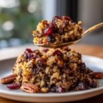 Ein L&ouml;ffel der leckeren Veganen Wildreis-F&uuml;llung wird &uuml;ber einem angerichteten Haufen auf einem Teller pr&auml;sentiert.