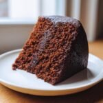 Nahaufnahme eines saftigen St&uuml;cks Veganer Schokoladenkuchen auf einem wei&szlig;en Teller.