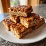 Stapel von z&auml;hen Flapjack Rezept St&uuml;cken, betr&auml;ufelt mit gl&auml;nzendem Karamell auf einem wei&szlig;en Teller.