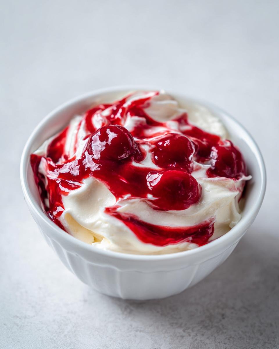 Nahaufnahme von cremigem Cherry Cheesecake Dip mit Kirschsauce und ganzen Kirschen in einer wei&szlig;en Schale.