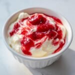 Nahaufnahme von cremigem Cherry Cheesecake Dip mit leuchtend roter Kirschsauce in einer wei&szlig;en Ramekin-Schale.