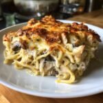 Ein cremiges St&uuml;ck Chicken Tetrazzini mit Spaghetti, Pilzen und &uuml;berbackener K&auml;sekruste auf einem wei&szlig;en Teller.