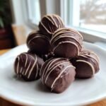 Ein Haufen von Chocolate Cherry Cheesecake Truffles, &uuml;berzogen mit dunkler Schokolade und wei&szlig;en Streifen, auf einem wei&szlig;en Teller.