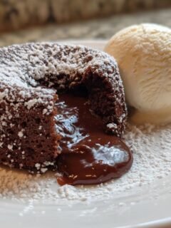 Ein saftiger Copycat Chilis Molten Lava Cake mit flüssigem Kern, bestäubt mit Puderzucker und einer Kugel Vanilleeis.