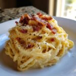 Nahaufnahme einer Portion cremiger Fettuccine Carbonara, garniert mit knusprigem Speck und schwarzem Pfeffer.