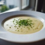Nahaufnahme einer cremigen, hellen Potato Soup, garniert mit frischem, gehacktem Schnittlauch.