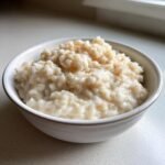 Nahaufnahme von cremigem Healthy Dairy Free Rice Pudding Recipe, bestreut mit Zimt, in einer wei&szlig;en Sch&uuml;ssel.