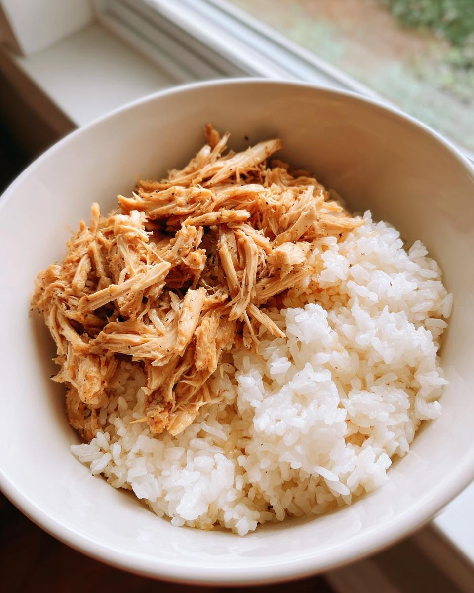 Nahaufnahme einer Sch&uuml;ssel mit wei&szlig;en Reis und gew&uuml;rztem, gezupftem H&auml;hnchen f&uuml;r Chicken Rice Bowls.