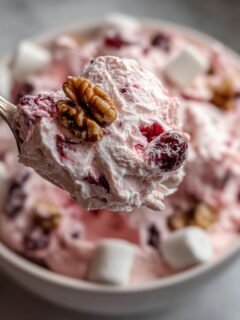 Ein L&ouml;ffel mit cremigem, rosa erfrischendes Cranberry Fluff Dessert, garniert mit Waln&uuml;ssen und Cranberrys.