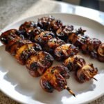 Nahaufnahme von glasierten, marinierten gegrillten Champignon Spie&szlig;en auf einem wei&szlig;en Teller.