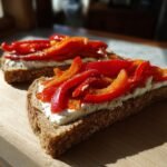 Zwei Scheiben Vollkornbrot belegt mit Frischk&auml;se und leuchtend roten Streifen von ger&ouml;steter Paprika f&uuml;r das Healthy Viral Bell Pepper Sandwich.