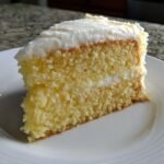 Nahaufnahme eines saftigen St&uuml;cks Italian Cream Sheet Cake mit cremiger F&uuml;llung und dicker wei&szlig;er Glasur.