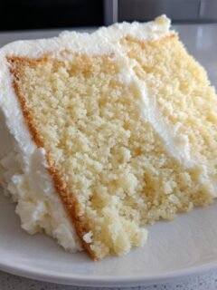 Nahaufnahme eines saftigen St&uuml;cks Italian Cream Sheet Cake mit dicker wei&szlig;er Creme-Glasur auf einem wei&szlig;en Teller.