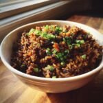 Eine wei&szlig;e Sch&uuml;ssel gef&uuml;llt mit dunklem Louisiana Dirty Rice, garniert mit frischem Schnittlauch.