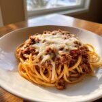 Nahaufnahme von Monterey Spaghetti mit Hackfleischsauce und geschmolzenem K&auml;se auf einem wei&szlig;en Teller.