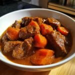 Nahaufnahme von Old Fashioned Beef Stew mit gro&szlig;en St&uuml;cken zartem Rindfleisch und leuchtend orangefarbenen Karotten in einer dunklen So&szlig;e in einer wei&szlig;en Sch&uuml;ssel.