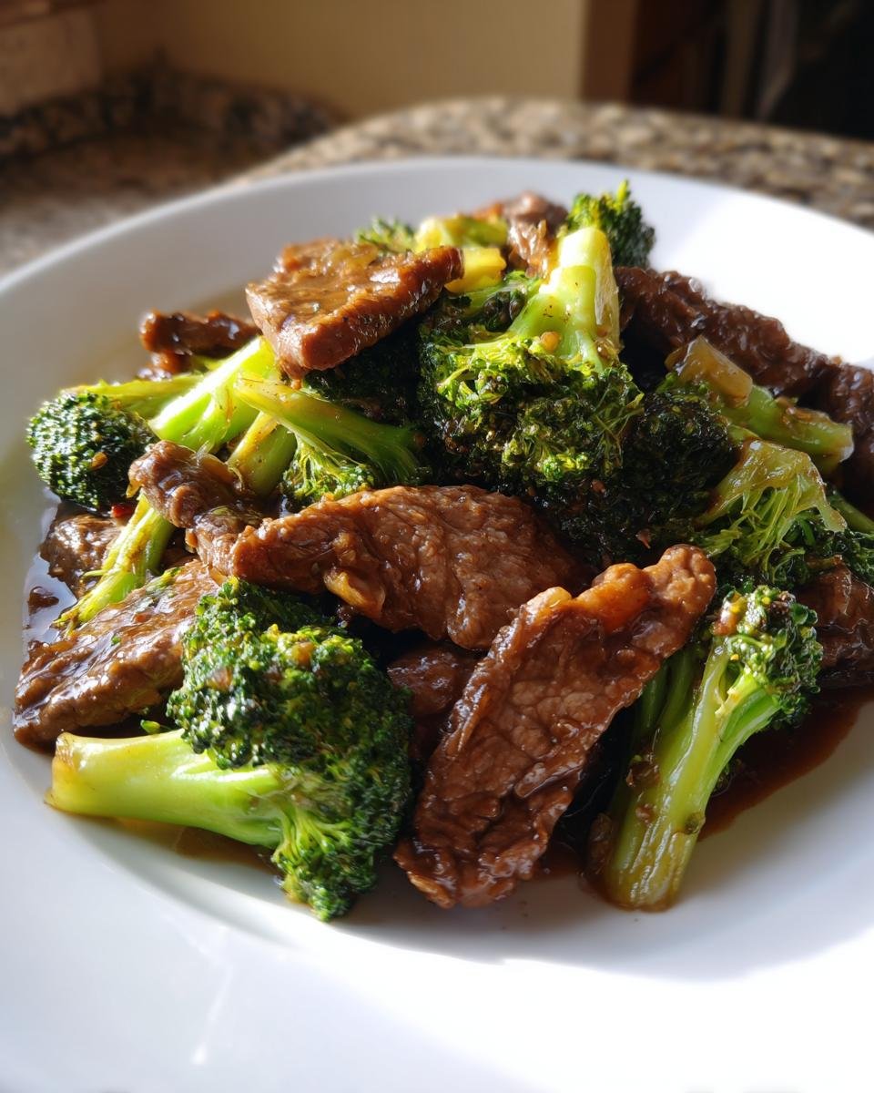 Nahaufnahme von saftigem Panda Express Beef And Broccoli mit gl&auml;nzender dunkler So&szlig;e auf einem wei&szlig;en Teller.