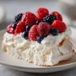 Nahaufnahme eines St&uuml;cks Pavlova Dessert mit knuspriger Baiserbasis, Schlagsahne und frischen roten und blauen Beeren.