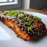Nahaufnahme eines saftigen Lachsfilets mit dunkler Teriyaki-Glasur, bestreut mit Sesam und Fr&uuml;hlingszwiebeln f&uuml;r das Quick Easy Baked Teriyaki Salmon Rezept.
