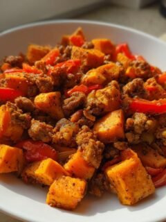 Nahaufnahme eines Quick Turkey Sweet Potato Skillet Recipe mit gew&uuml;rfelten S&uuml;&szlig;kartoffeln, Hackfleisch und roten Paprikastreifen in einer wei&szlig;en Sch&uuml;ssel.