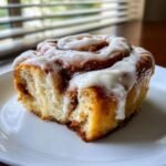 Nahaufnahme einer saftigen Pumpkin Cinnamon Rolls mit reichlich wei&szlig;em Zuckerguss auf einem wei&szlig;en Teller.