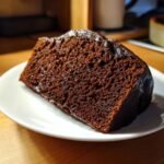 Nahaufnahme eines saftigen St&uuml;cks Chocolate Buttermilk Cake auf einem wei&szlig;en Teller.