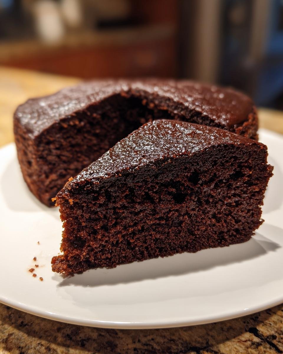 Nahaufnahme eines saftigen St&uuml;cks Chocolate Buttermilk Cake auf einem wei&szlig;en Teller.