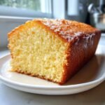 Nahaufnahme eines saftigen St&uuml;cks Vanilla Buttermilk Cake mit goldbrauner Kruste und Glasur auf einem wei&szlig;en Teller.