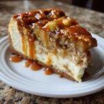 Ein cremiges St&uuml;ck Salted Caramel Apple Pie Cheesecake mit Karamellso&szlig;e auf einem wei&szlig;en Teller.