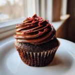 Nahaufnahme eines dunklen Schokoladen-Cupcakes mit reichhaltigem Schokoladenfrosting und roten Streuseln, perfekt f&uuml;r Valentine Cupcakes.