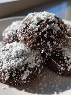 Nahaufnahme von mehreren dunklen Schokoladen-Schneeb&auml;llchen Keksen, reichlich mit Puderzucker best&auml;ubt.