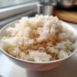 Nahaufnahme von fluffigem, wei&szlig;em Coconut Rice in einer wei&szlig;en Sch&uuml;ssel, bereit zum Servieren.