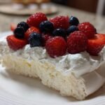 Nahaufnahme eines St&uuml;cks Pavlova Dessert mit luftiger Baiserbasis, Schlagsahne und frischen roten Beeren.