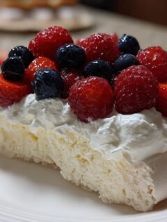 Nahaufnahme eines Stücks Pavlova Dessert mit luftiger Baiserbasis, Schlagsahne und frischen roten Beeren.