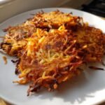 Drei goldbraun gebratene Sweet Potato Hash Browns mit knusprigen R&auml;ndern auf einem wei&szlig;en Teller.