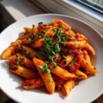 Nahaufnahme von Penne Arrabbiata in einer wei&szlig;en Sch&uuml;ssel, bedeckt mit scharfer Tomatensauce und frischer Petersilie.