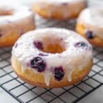 Nahaufnahme eines glasierten Air Fryer Blueberry Donuts mit sichtbaren Blaubeeren auf einem K&uuml;hlrost.