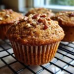 Nahaufnahme eines saftigen Banana Cinnamon Pecan Cupcakes, garniert mit Pekann&uuml;ssen auf einem Gitter.