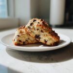 Zwei aufgeschnittene Chocolate Chip Coffee Scones mit Schokoladenst&uuml;ckchen auf einem wei&szlig;en Teller.