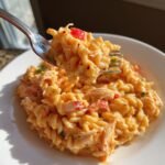 Gabel mit cremigem Cajun Krabben Nudelsalat, reich an Sauce und roten Paprikast&uuml;cken.