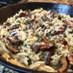 Nahaufnahme von cremiger Pilz-Orzo-Pfanne mit gebratenen Pilzen und Parmesan.